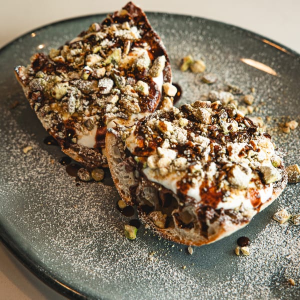 Two halves of a Boa's CVC dessert, topped with cream, chocolate drizzle, and nuts on a dark plate.