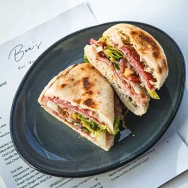 A Boa's CVC cafe sandwich, cut in half, filled with meat, cheese, and lettuce on a dark plate.