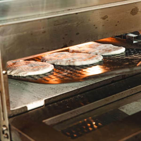 Pita bread baking on a conveyor belt inside a hot oven at Boa's CVC cafe.