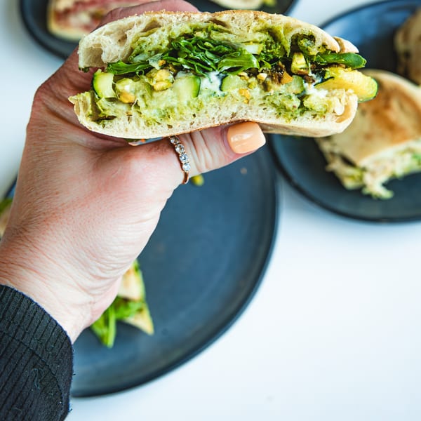 A hand holding a Boa's CVC cafe sandwich filled with green vegetables and sauce.