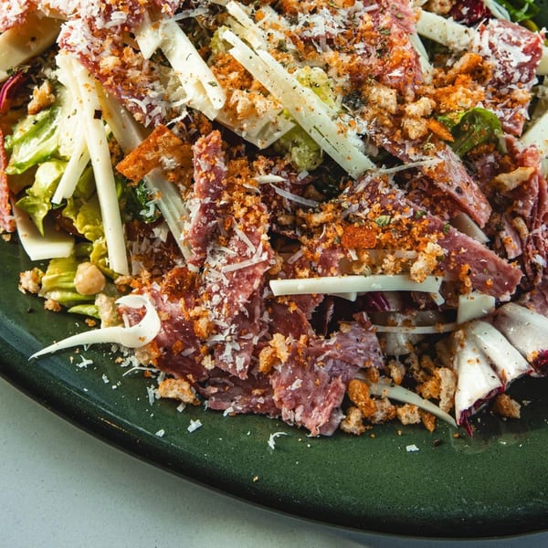 Close-up of a Boa's CVC cafe salad with salami, cheese, croutons, and greens on a green plate.