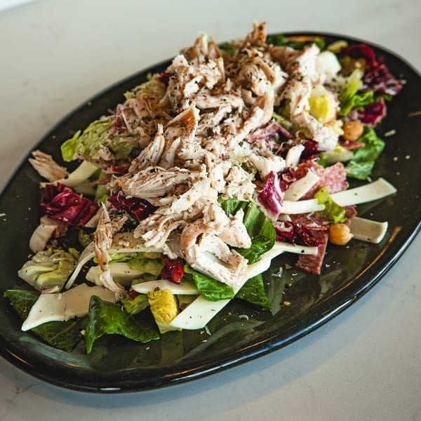 A Boa's CVC cafe salad with shredded chicken, mixed greens, cheese, and salami on a dark plate.